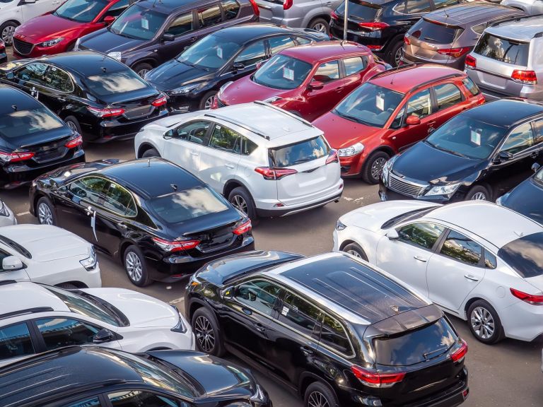 Sale of new and used cars in a dealership. Lots of cars in the car park. Black, white, silver and red cars of unknown brands.