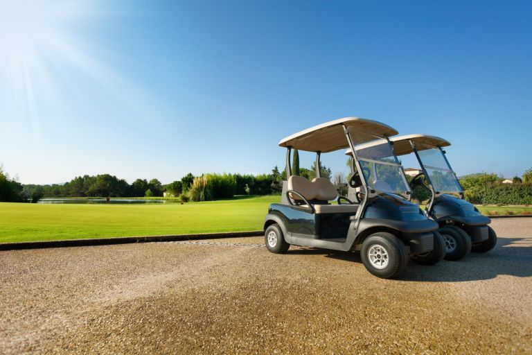 Two golf-carts standing at the parking lots against green golf course