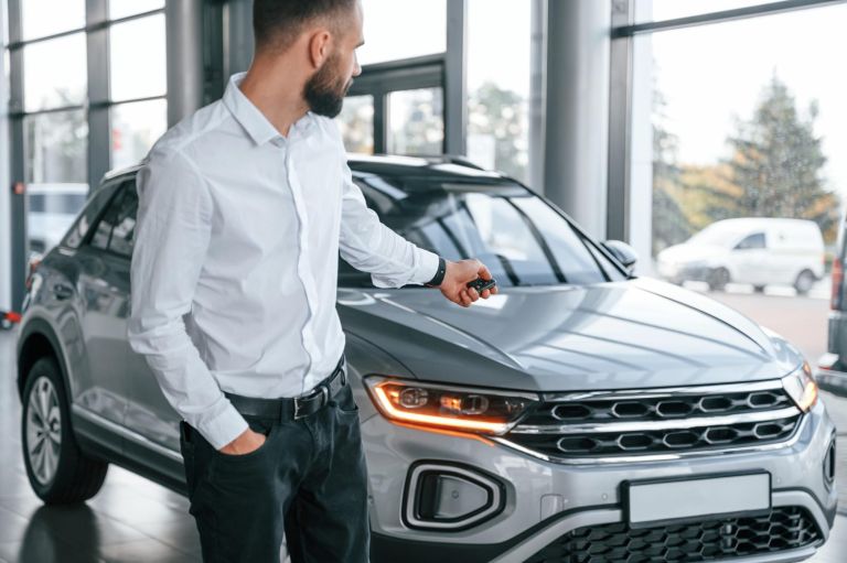 Closing the automobile by remote keys. Young man in white clothes is in the car dealership.