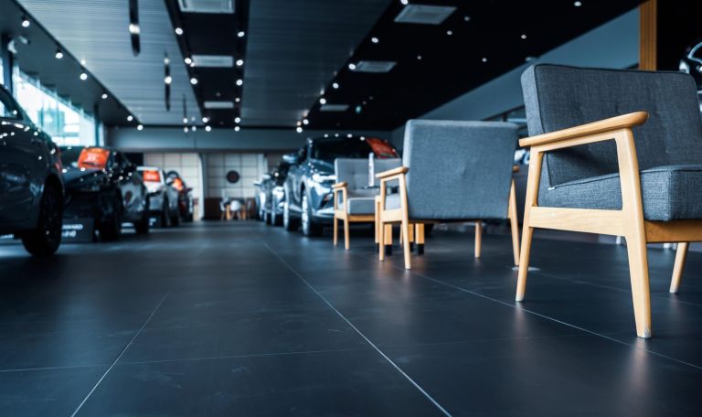 Luxury showroom interior. Car dealership office. New car parked in modern showroom and chairs for customer service. Car for sale and rent business concept. Automobile leasing and insurance background.