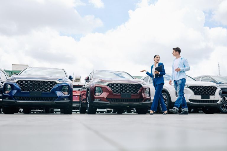 Positive female car dealership saleswoman walking along rows of new cars with customer