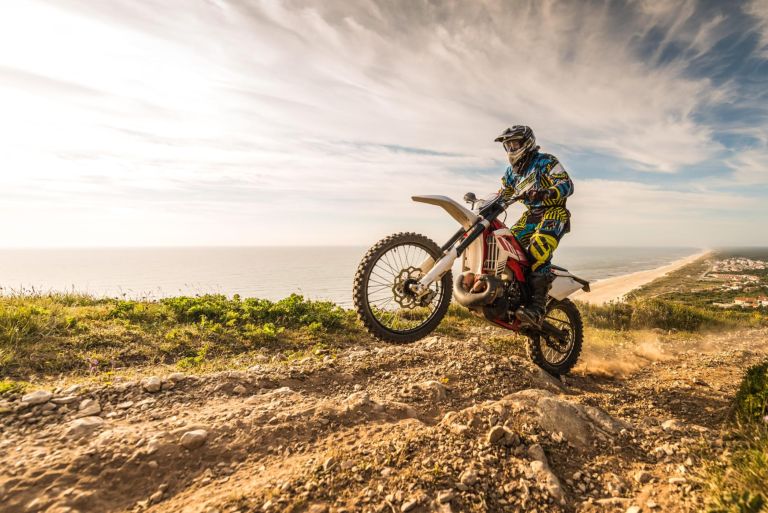 Enduro rider climbing a steep slope against a beautiful sunset on a seascape