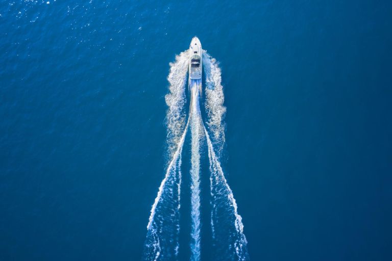 Drone view of a boat sailing. Top view of a white boat sailing to the blue sea. Motor boat in the sea. Travel - image.