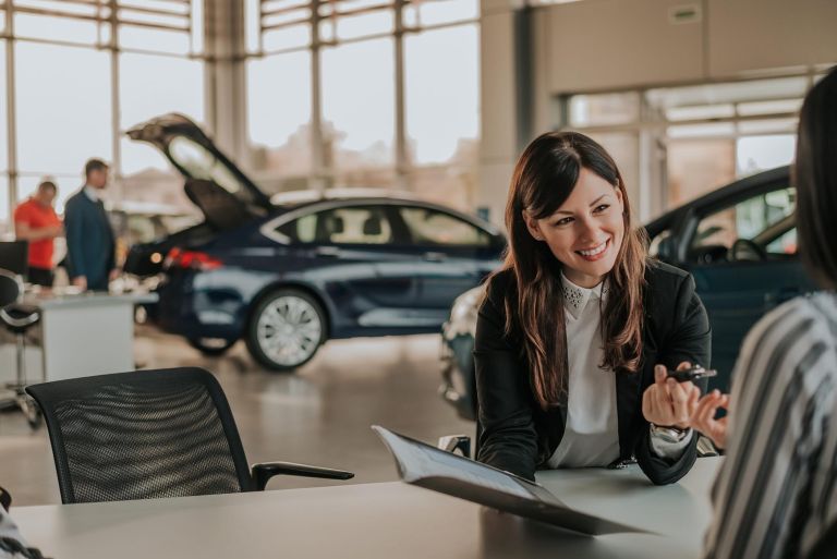 Cheerful car dealer showing files and giving keys to client.
