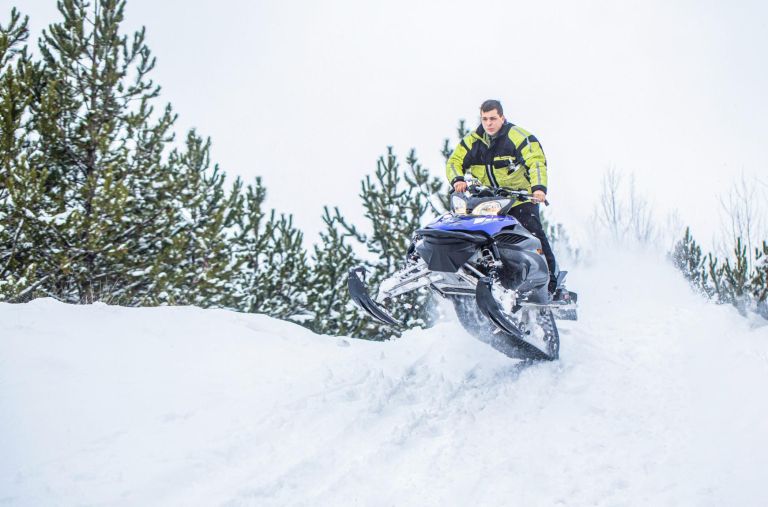 Jumping on a snowmobile on a background of winter forest. Bright snowmobile. Athlete on a snowmobile moving in the winter forest in the mountains. Man and fast action snowmobile jumping.