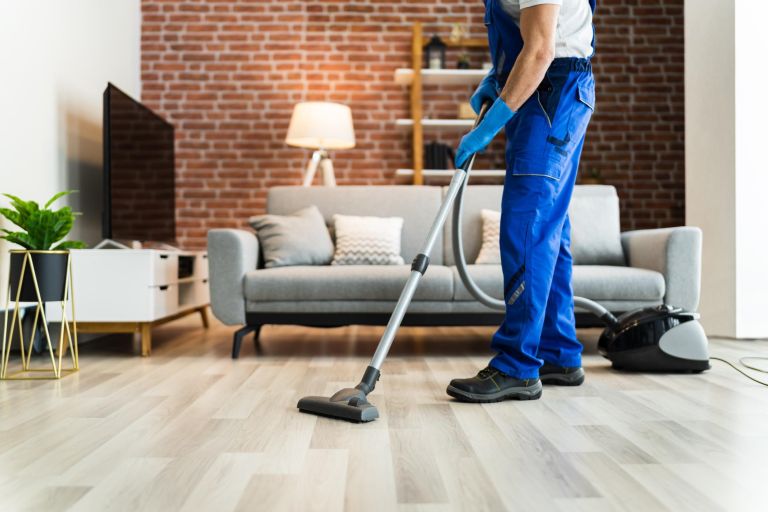Man In Uniform Vacuuming House Floor. Cleaning Home