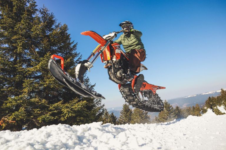 Snowbike rider in mountain valley in beautiful snow powder. Snowdirt bike with splashes and trail. Snowmobile winter sport riding