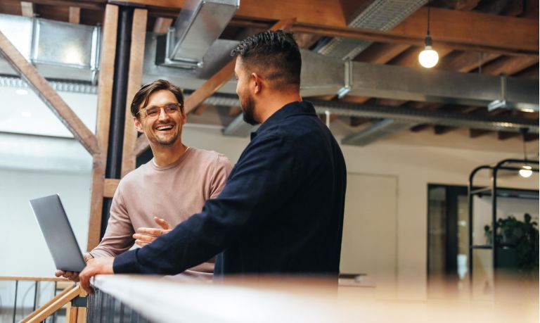 Two business men talking to each other about their tech work. Business colleagues discussing efficient ideas to finish a project. Male professionals working in a startup.