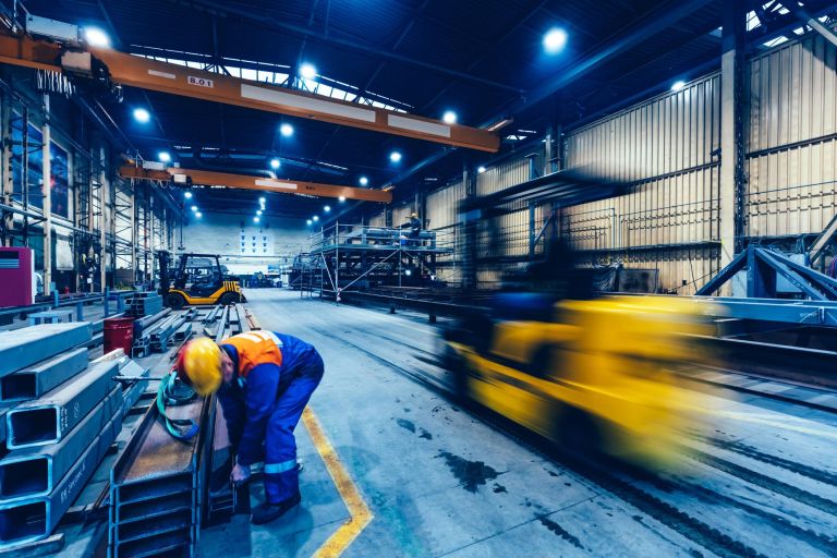 Factory work. Forklift moving and a blue-collar worker taking a steel profile. Shipyard, heavy industry