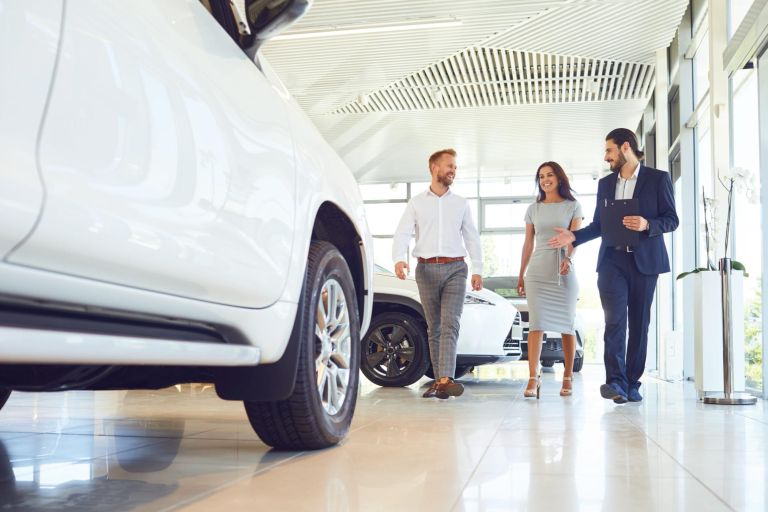 Happy couple and the dealer selling cars look the car in the showroom. Buying rental a car.